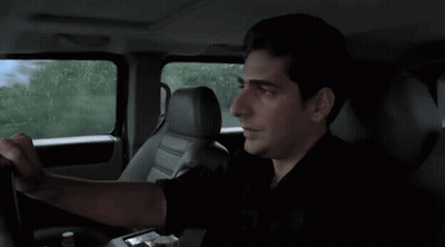A Man In A Black Shirt Is Driving A Car With A Mountain In The Background GIF