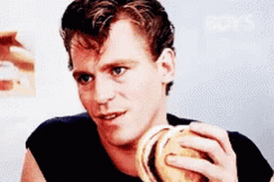 A Man In A Black Shirt Is Eating A Burger GIF
