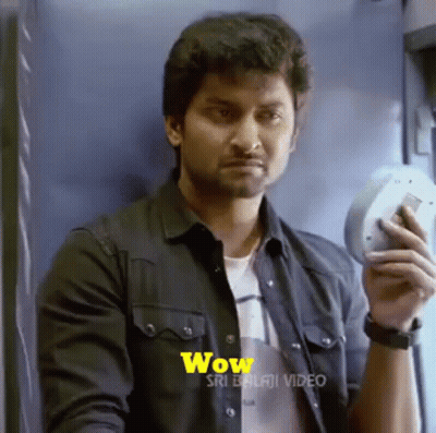 A Man In A Black Shirt Is Holding A Cell Phone In His Hand And Making A Surprised Face . GIF