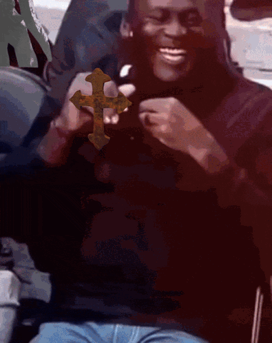 A Man In A Black Shirt Is Holding A Cross In His Hands And Smiling GIF