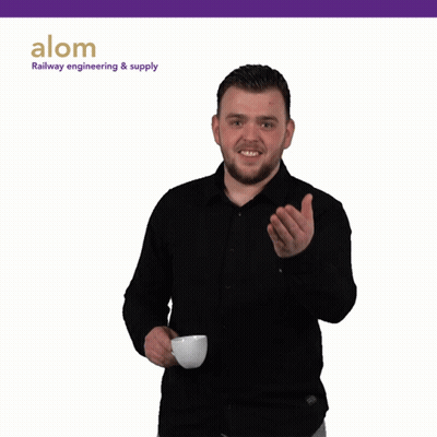 A Man In A Black Shirt Is Holding A Cup Of Coffee In Front Of A Sign That Says Alom GIF