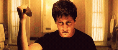 A Man In A Black Shirt Is Holding A Hammer In His Hand . GIF