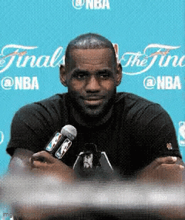 A Man In A Black Shirt Is Holding A Microphone In Front Of A Sign That Says Nba GIF