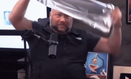 A Man In A Black Shirt Is Holding A Piece Of Aluminum Foil Over His Head In Front Of A Microphone GIF