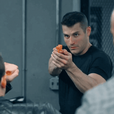 A Man In A Black Shirt Is Holding A Small Orange Object In His Hand GIF