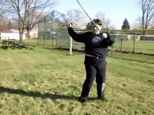 A Man In A Black Shirt Is Holding A Sword In A Field GIF