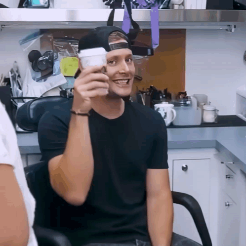 A Man In A Black Shirt Is Holding A White Cup GIF