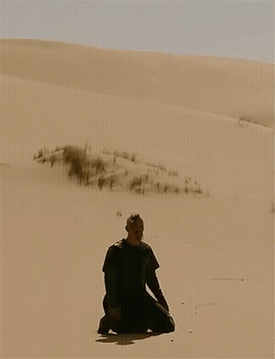 A Man In A Black Shirt Is Kneeling In The Sand GIF