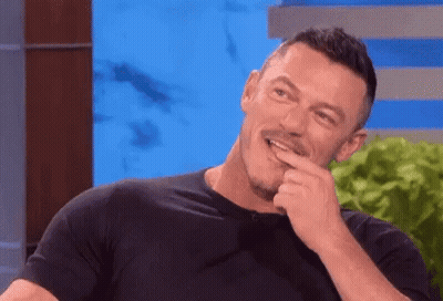 A Man In A Black Shirt Is Laughing With His Hand To His Mouth . GIF