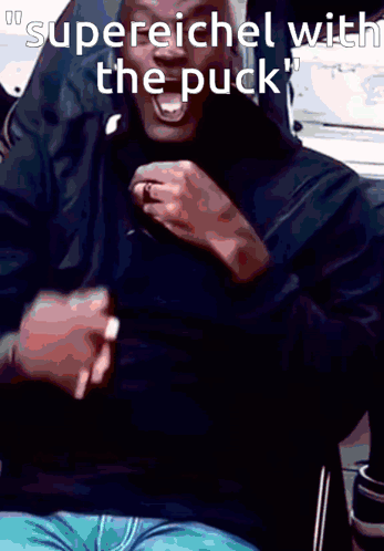 A Man In A Black Shirt Is Laughing With The Words Supereichel With The Puck Below Him GIF