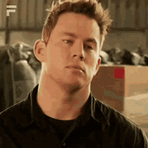 A Man In A Black Shirt Is Making A Funny Face In A Warehouse . GIF