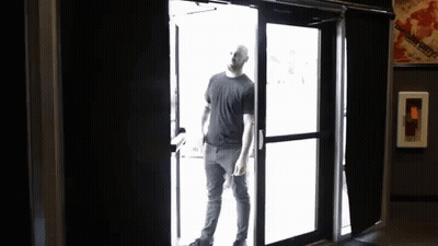 A Man In A Black Shirt Is Opening A Door GIF