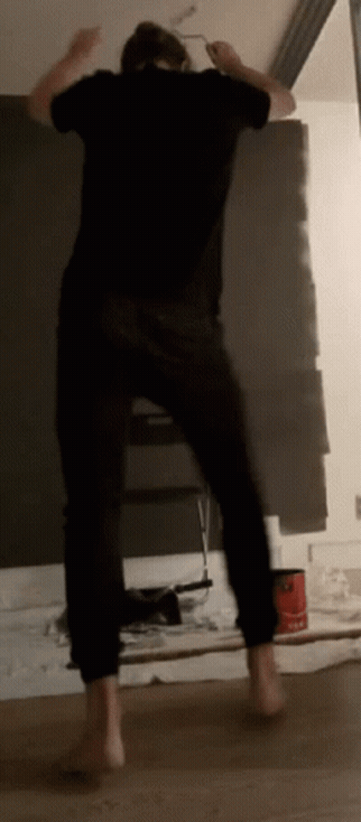 A Man In A Black Shirt Is Painting A Wall With A Brush GIF