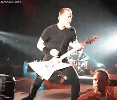 A Man In A Black Shirt Is Playing A Guitar On A Stage GIF