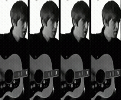 A Man In A Black Shirt Is Playing An Acoustic Guitar In A Black And White Photo GIF