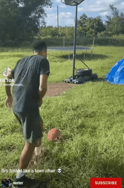 A Man In A Black Shirt Is Playing Basketball In A Field With A Trampoline In The Background GIF