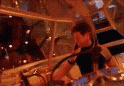 A Man In A Black Shirt Is Playing Drums In A Room . GIF