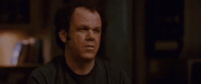A Man In A Black Shirt Is Sitting At A Table In A Dark Room . GIF