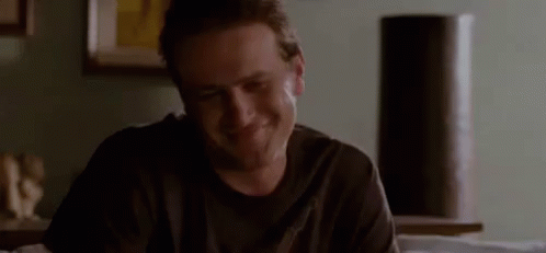 A Man In A Black Shirt Is Sitting At A Table In A Living Room And Smiling . GIF
