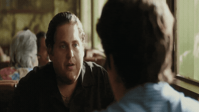 A Man In A Black Shirt Is Sitting At A Table Talking To Another Man GIF
