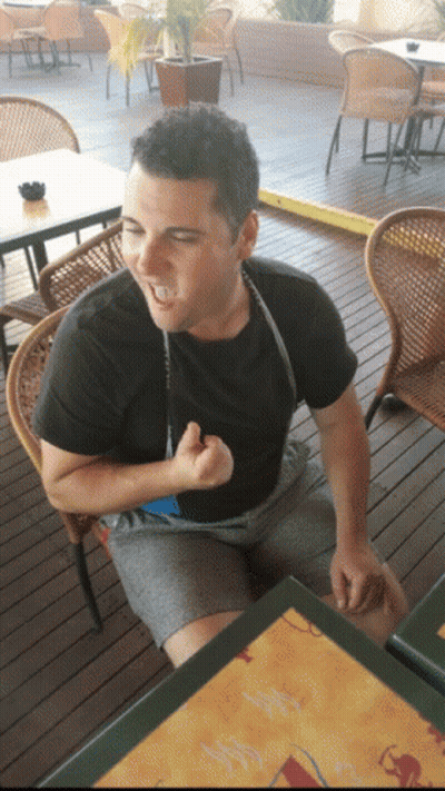 A Man In A Black Shirt Is Sitting At A Table With A Menu On It GIF