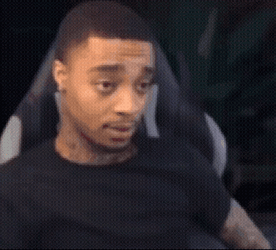 A Man In A Black Shirt Is Sitting In A Chair And Looking At The Camera . GIF