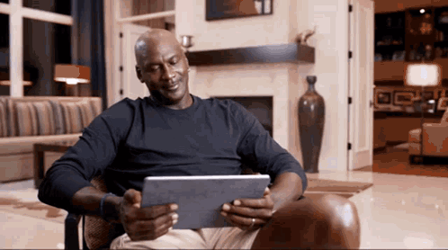 A Man In A Black Shirt Is Sitting In A Chair Using A Tablet GIF