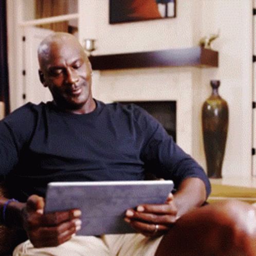 A Man In A Black Shirt Is Sitting In A Chair Using A Tablet GIF