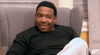 A Man In A Black Shirt Is Sitting In A Chair With A Mtv Logo In The Background GIF