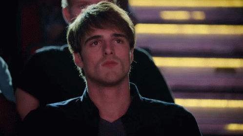 A Man In A Black Shirt Is Sitting In A Dark Room With Stairs In The Background GIF