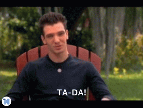 A Man In A Black Shirt Is Sitting In A Red Chair And Says Ta-Da . GIF