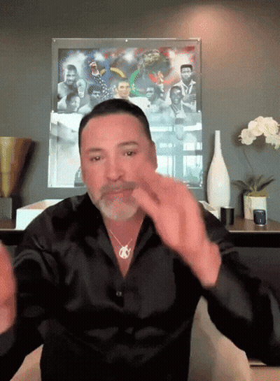 A Man In A Black Shirt Is Sitting In Front Of A Framed Picture GIF