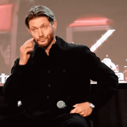 A Man In A Black Shirt Is Sitting In Front Of A Microphone And Making A Face GIF