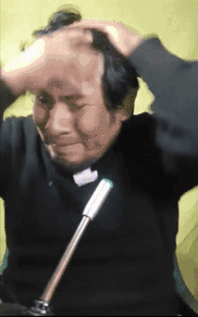 A Man In A Black Shirt Is Sitting In Front Of A Microphone And Scratching His Head GIF