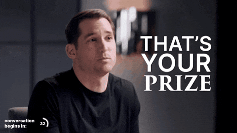 A Man In A Black Shirt Is Sitting In Front Of A Sign That Says That 'S Your Prize GIF