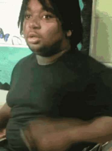 A Man In A Black Shirt Is Sitting In Front Of A Wall With Butterflies On It GIF