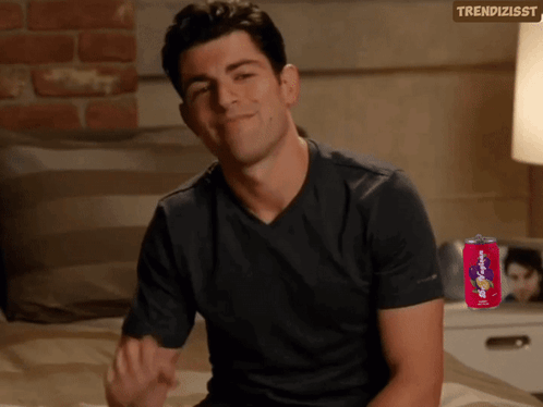 A Man In A Black Shirt Is Sitting On A Bed Next To A Can Of Soda GIF
