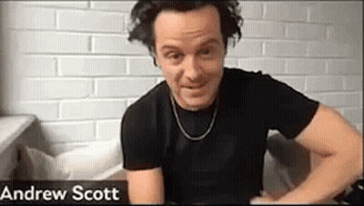 A Man In A Black Shirt Is Sitting On A Couch In Front Of A Brick Wall . GIF