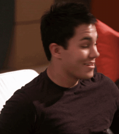 A Man In A Black Shirt Is Sitting On A Couch Smiling GIF