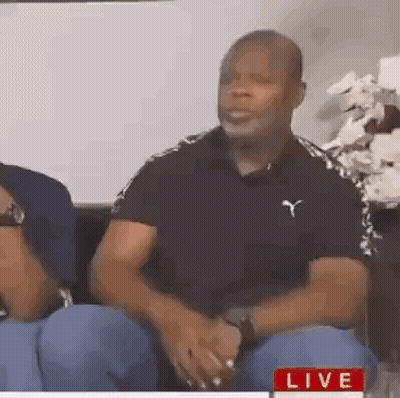 A Man In A Black Shirt Is Sitting On A Couch With A Woman . GIF