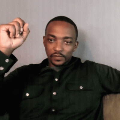 A Man In A Black Shirt Is Sitting On A Couch With His Fist Up GIF