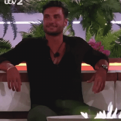 A Man In A Black Shirt Is Sitting On A Couch With His Hands Folded . GIF