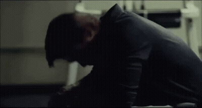 A Man In A Black Shirt Is Sitting On The Floor With His Head On His Knees . GIF
