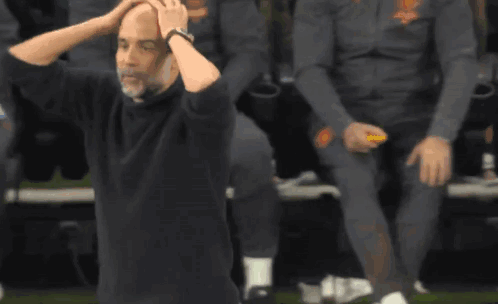A Man In A Black Shirt Is Sitting On The Ground With His Hands On His Head . GIF