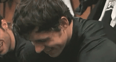 A Man In A Black Shirt Is Smiling And Looking At The Camera . GIF