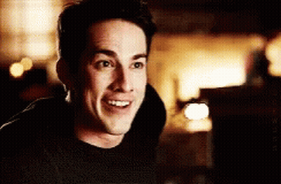 A Man In A Black Shirt Is Smiling In A Dark Room . GIF
