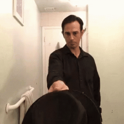 A Man In A Black Shirt Is Standing In A Bathroom With A Towel Rack . GIF