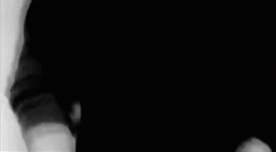 A Man In A Black Shirt Is Standing In A Black And White Photo . GIF