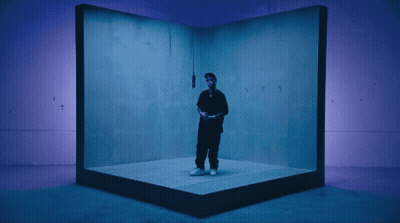 A Man In A Black Shirt Is Standing In A Blue Room GIF