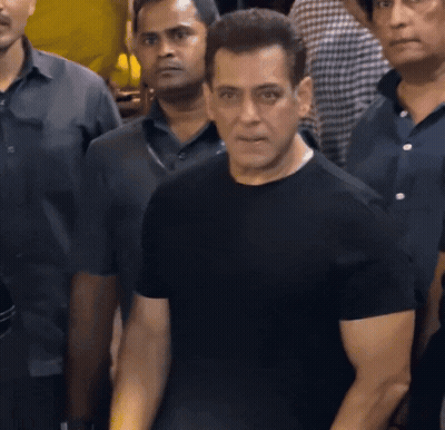 A Man In A Black Shirt Is Standing In A Crowd Of People GIF